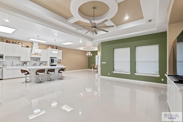 kitchen featuring sink, tasteful backsplash, hanging light fixtures, ceiling fan with notable chandelier, and white cabinets