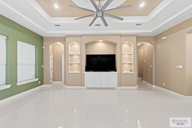 unfurnished living room with a raised ceiling, light tile patterned floors, ceiling fan, and built in shelves