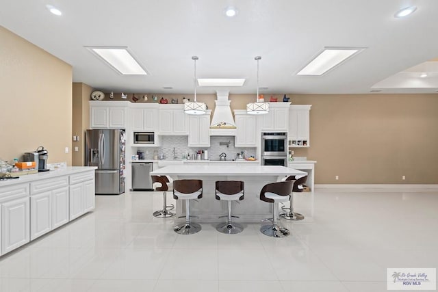 kitchen featuring appliances with stainless steel finishes, hanging light fixtures, tasteful backsplash, white cabinets, and a kitchen island