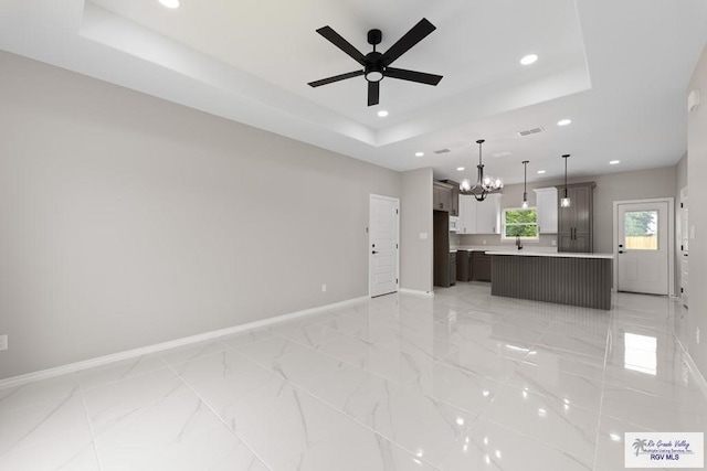 kitchen featuring white cabinetry, pendant lighting, a tray ceiling, a kitchen island, and ceiling fan with notable chandelier