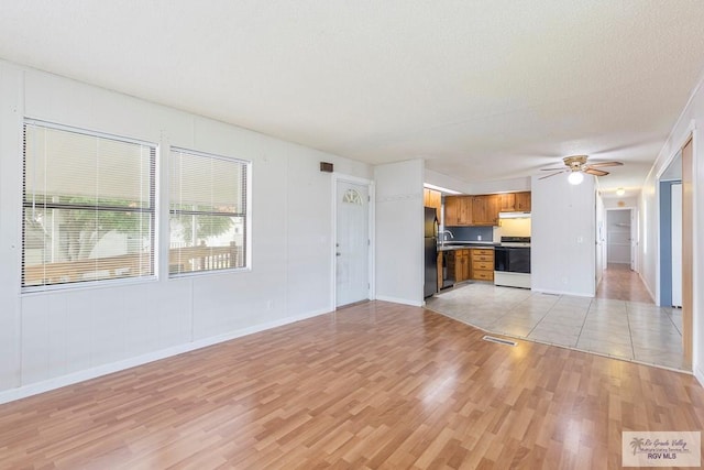 unfurnished living room with ceiling fan, a textured ceiling, and light hardwood / wood-style flooring