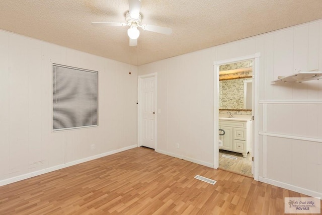 unfurnished bedroom featuring a textured ceiling, ceiling fan, sink, light hardwood / wood-style flooring, and connected bathroom