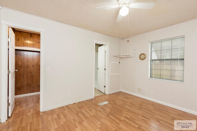 empty room featuring wood walls, ceiling fan, a textured ceiling, and light wood-type flooring