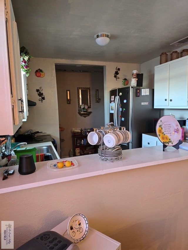 kitchen with kitchen peninsula, stainless steel fridge with ice dispenser, white cabinetry, and sink