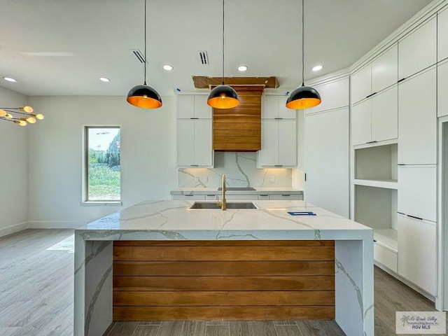 kitchen with white cabinetry, an island with sink, hanging light fixtures, and light hardwood / wood-style flooring