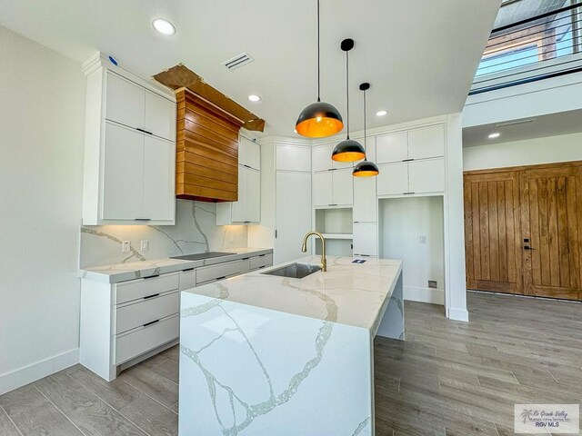 kitchen with white cabinetry, sink, a large island, light hardwood / wood-style flooring, and pendant lighting