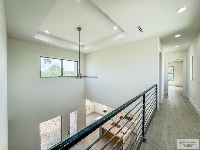 hallway featuring light wood-type flooring and a raised ceiling