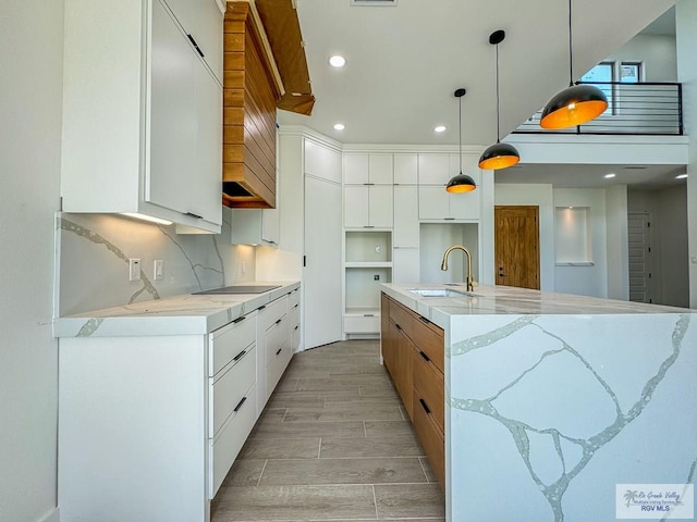 kitchen featuring sink, decorative light fixtures, light hardwood / wood-style floors, white cabinetry, and a large island