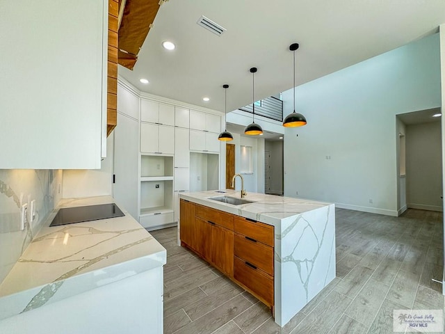 kitchen with sink, an island with sink, pendant lighting, light hardwood / wood-style floors, and white cabinets