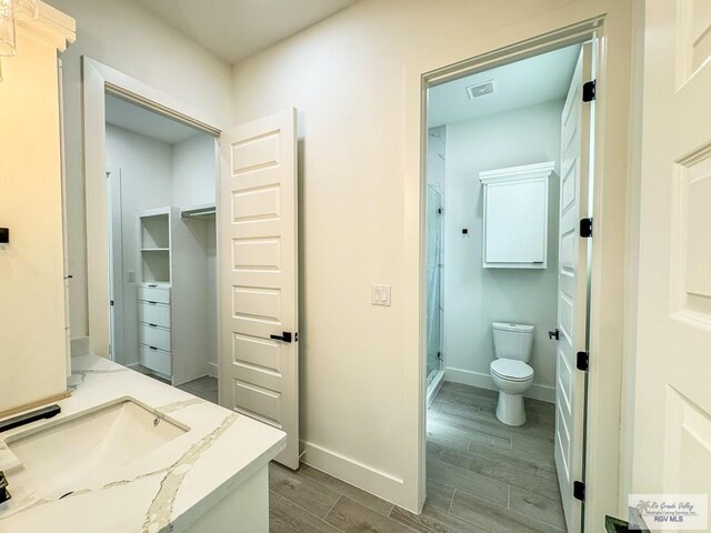 bathroom with walk in shower, vanity, wood-type flooring, and toilet