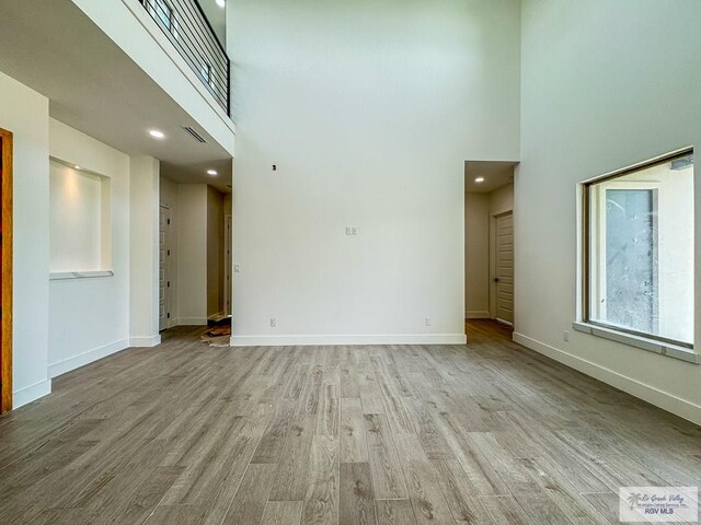 unfurnished living room featuring a towering ceiling and light wood-type flooring