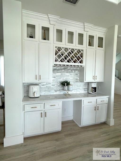 bar with tasteful backsplash, white cabinets, and light wood-type flooring