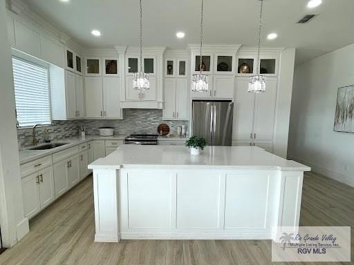 kitchen featuring sink, stainless steel appliances, a kitchen island, pendant lighting, and white cabinets