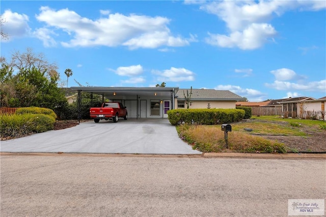 view of front facade featuring an attached carport, concrete driveway, and fence