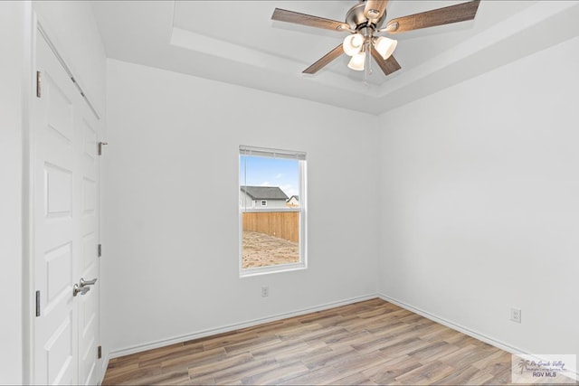 empty room featuring ceiling fan, a raised ceiling, and light wood-type flooring