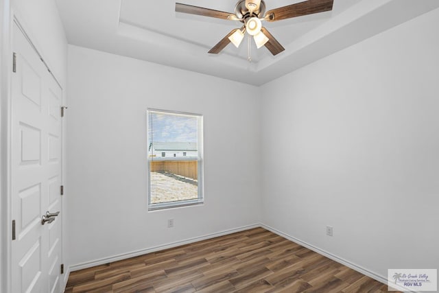 empty room with a raised ceiling, ceiling fan, and dark wood-type flooring