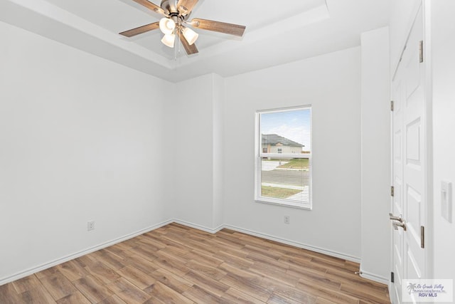 empty room with ceiling fan, light hardwood / wood-style flooring, and a tray ceiling