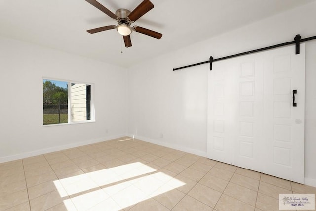 tiled empty room featuring a barn door and ceiling fan