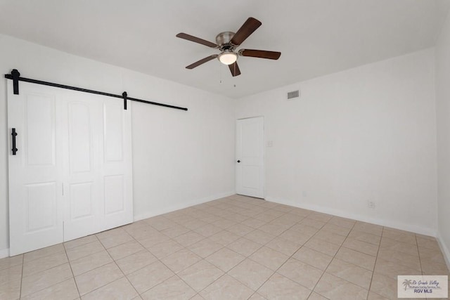 unfurnished bedroom featuring a barn door, ceiling fan, a closet, and light tile patterned flooring