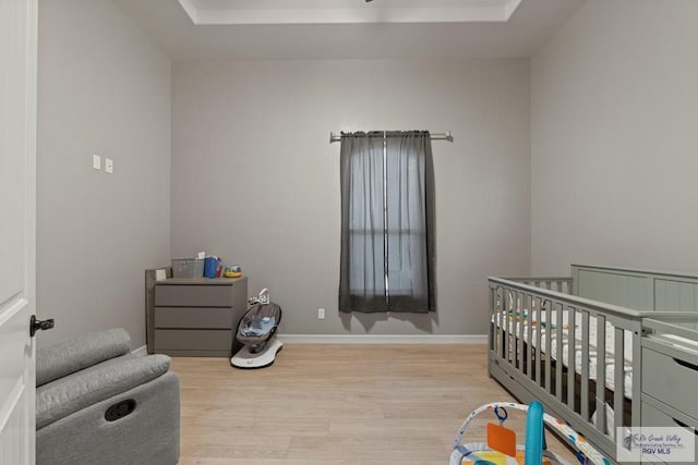 bedroom with a raised ceiling, light hardwood / wood-style flooring, and a nursery area