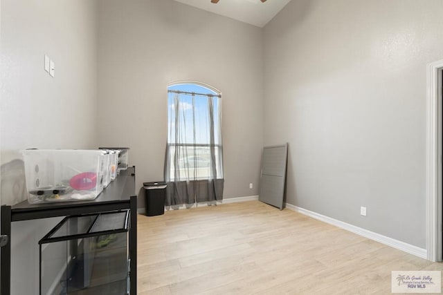 miscellaneous room with ceiling fan, light wood-type flooring, and a towering ceiling