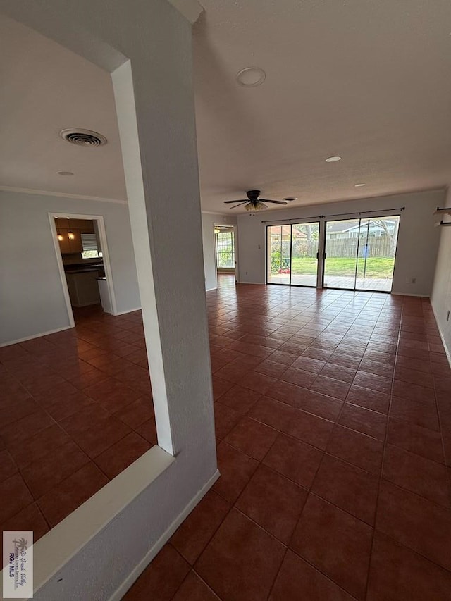 spare room with crown molding, visible vents, ceiling fan, dark tile patterned flooring, and baseboards