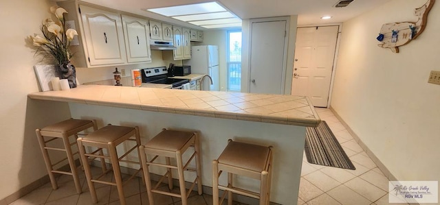 kitchen with tile counters, kitchen peninsula, a breakfast bar, light tile patterned flooring, and black appliances