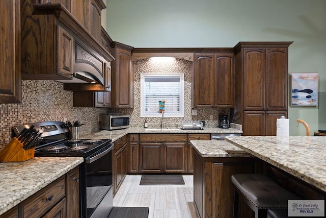 kitchen featuring dark brown cabinetry, sink, tasteful backsplash, light stone counters, and appliances with stainless steel finishes