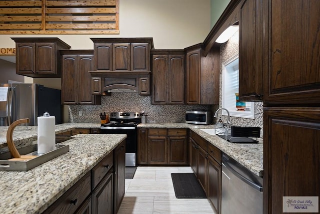 kitchen featuring appliances with stainless steel finishes, backsplash, light stone counters, and dark brown cabinetry