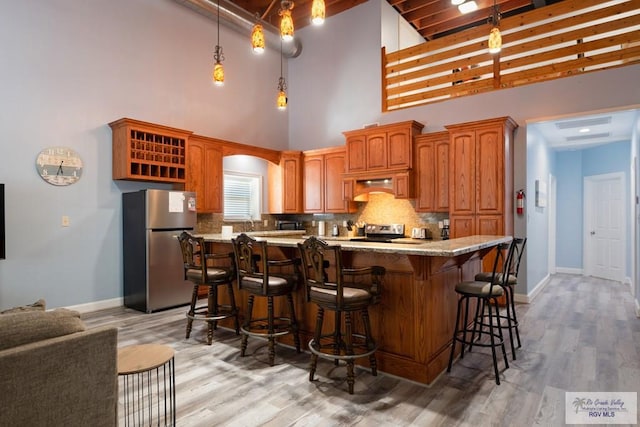 kitchen with tasteful backsplash, stainless steel appliances, beamed ceiling, a high ceiling, and light hardwood / wood-style floors