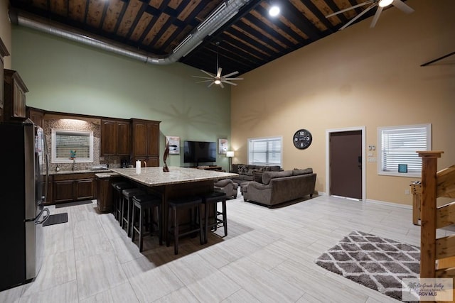 kitchen with a towering ceiling, a kitchen island, wood ceiling, a breakfast bar area, and stainless steel refrigerator