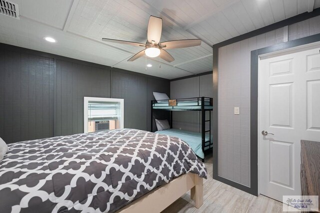 bedroom with ceiling fan, light hardwood / wood-style flooring, and wood walls