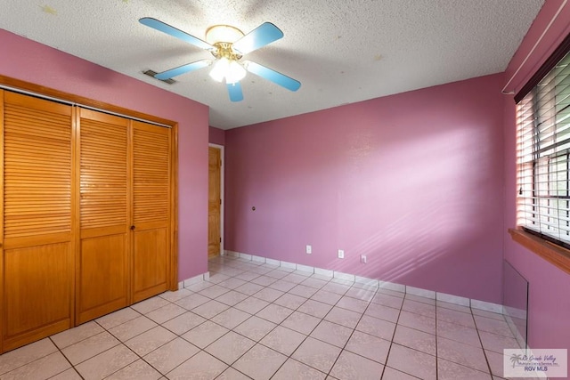 unfurnished bedroom featuring ceiling fan, a closet, light tile patterned flooring, and a textured ceiling