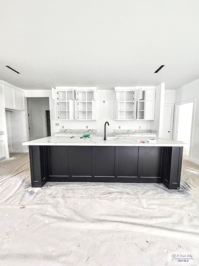 kitchen with white cabinetry, sink, and a large island with sink