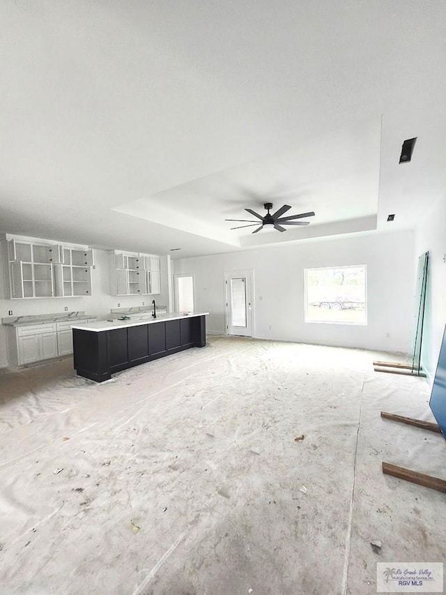 unfurnished living room with sink, a raised ceiling, and ceiling fan