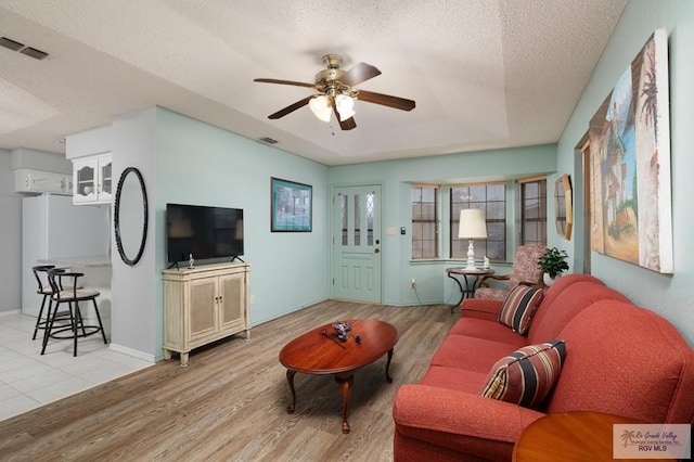 living room with ceiling fan, a raised ceiling, a textured ceiling, and light wood-type flooring