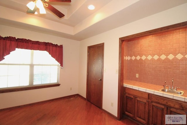 unfurnished bedroom featuring hardwood / wood-style floors, ceiling fan, indoor wet bar, and a tray ceiling