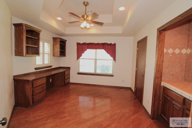 interior space featuring a tray ceiling, ceiling fan, tile counters, and a healthy amount of sunlight