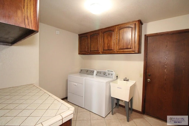 clothes washing area with cabinets, light tile patterned floors, and washing machine and clothes dryer