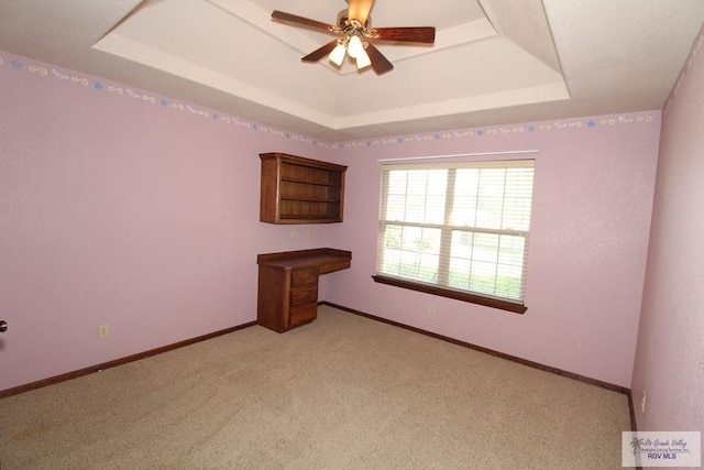 carpeted spare room with a raised ceiling and ceiling fan