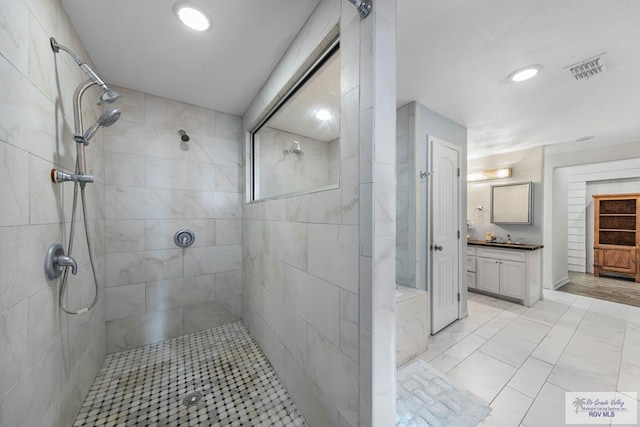 bathroom with a tile shower and vanity