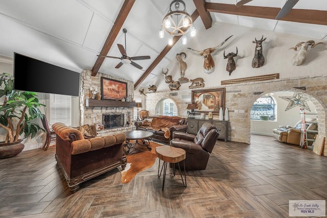 living room with ceiling fan, a stone fireplace, dark parquet floors, beamed ceiling, and high vaulted ceiling