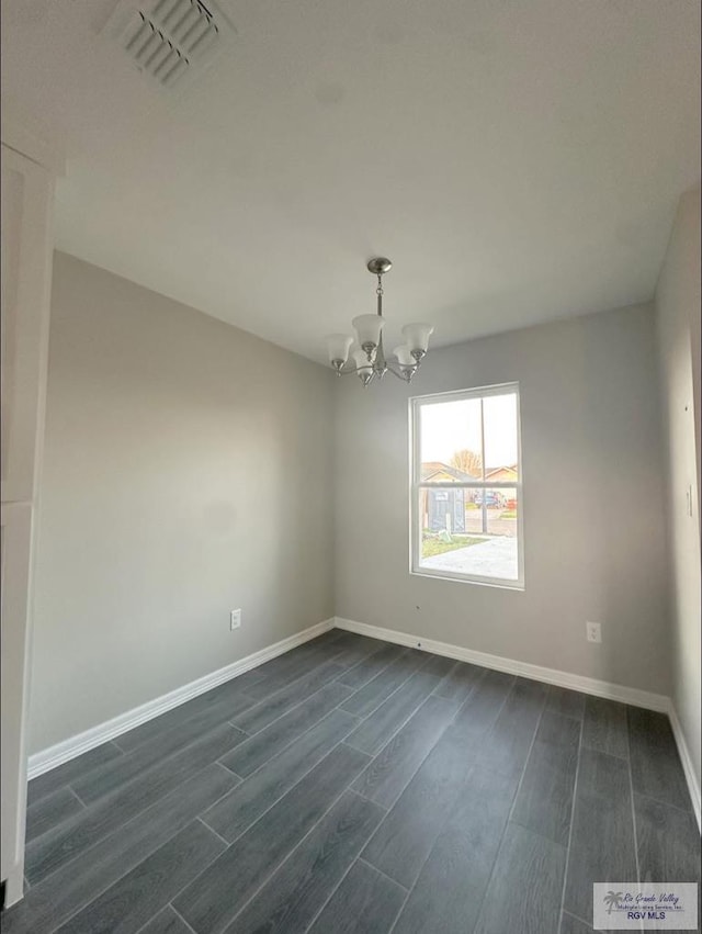 empty room featuring dark wood-type flooring and a notable chandelier