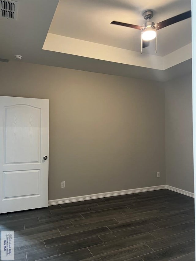 empty room with a raised ceiling, ceiling fan, and dark hardwood / wood-style flooring