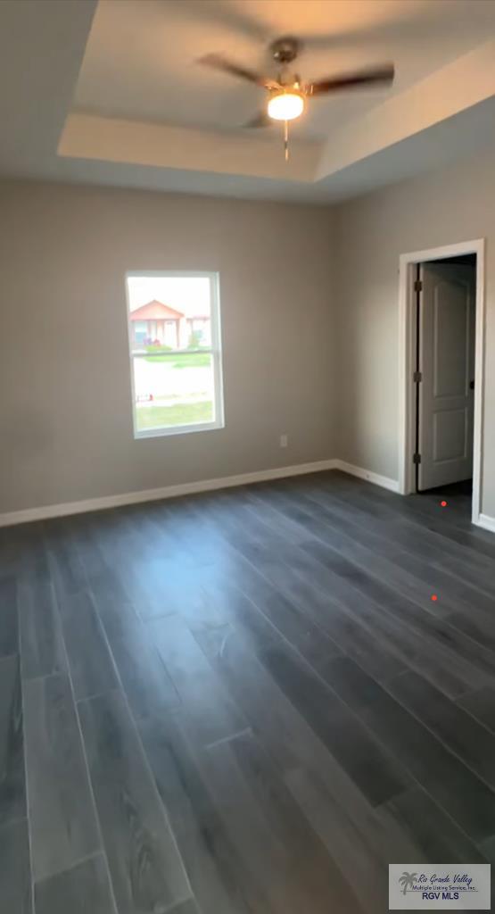 empty room featuring a tray ceiling, ceiling fan, and dark hardwood / wood-style floors