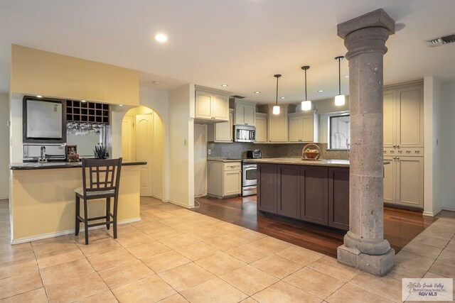 kitchen featuring light hardwood / wood-style flooring, ornate columns, appliances with stainless steel finishes, cream cabinetry, and decorative light fixtures