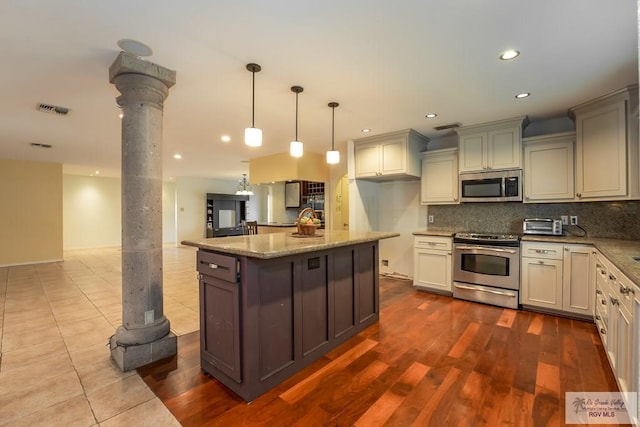 kitchen featuring ornate columns, stainless steel appliances, light stone counters, hardwood / wood-style floors, and decorative backsplash