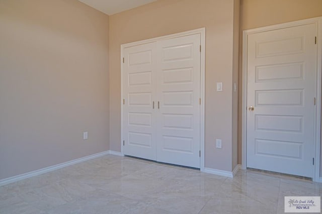 unfurnished bedroom with marble finish floor, baseboards, and a closet