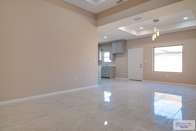 unfurnished living room with baseboards, a raised ceiling, a sink, and recessed lighting