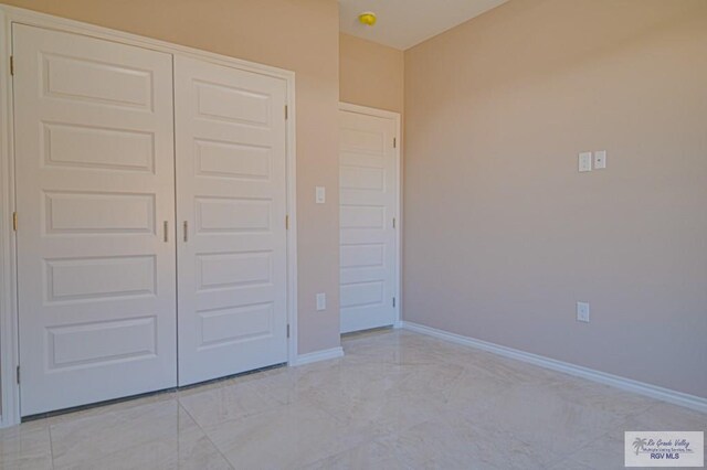 unfurnished bedroom featuring marble finish floor, baseboards, and a closet